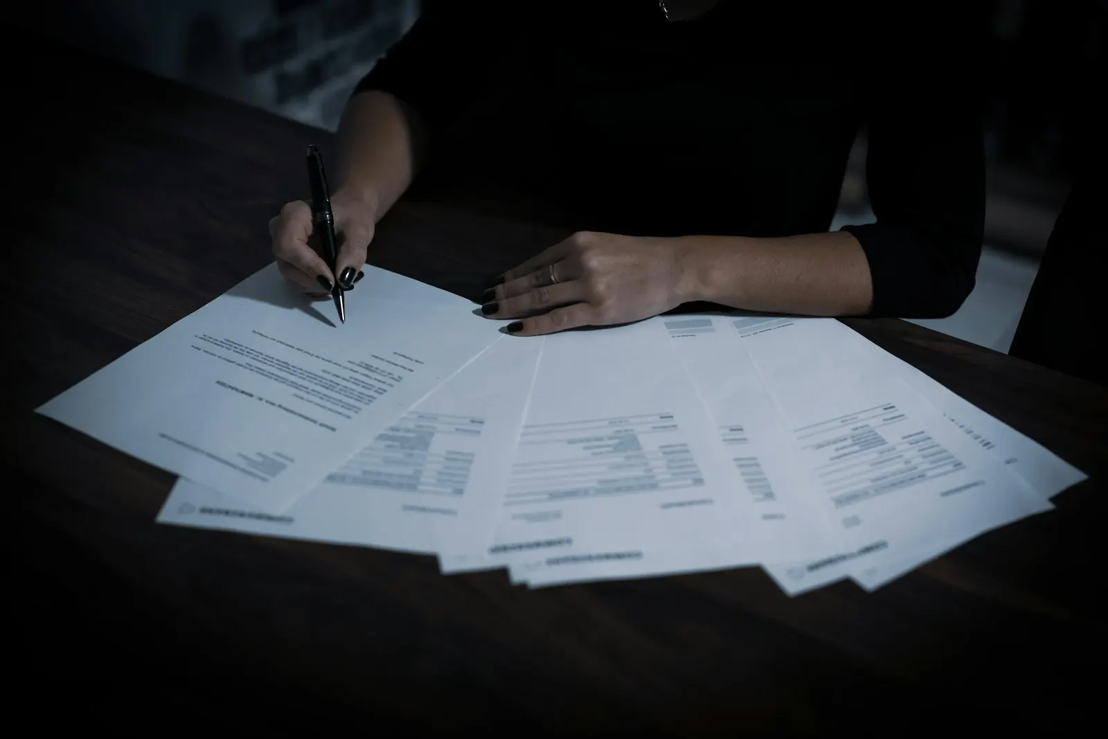 A person signing one of several printed quotes fanned out across a desk